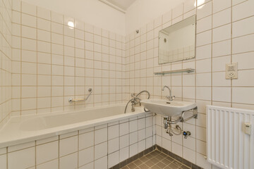 A clean and minimalistic bathroom featuring white tiled walls, a bathtub, sink, and a large mirror, emphasizing simplicity and functionality.