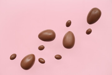 Tasty chocolate eggs flying on pink background