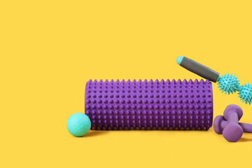 Massage rollers with ball and dumbbells on yellow background