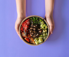 A hand holding a vibrant poke bowl with fresh ingredients, including salmon, avocado, seaweed, and...