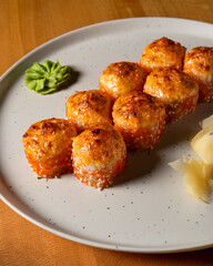 Baked sushi rolls with a golden, crispy topping, served on a white plate with wasabi and pickled ginger. Japanese cuisine, close-up view, warm lighting.