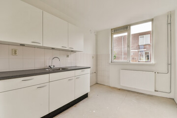 A bright and spacious kitchen features sleek white cabinetry, a minimalist design, and ample natural light from a large window. Perfect for modern living.