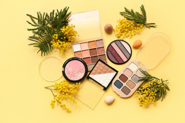 Decorative cosmetics with makeup sponges and mimosa flowers on yellow background