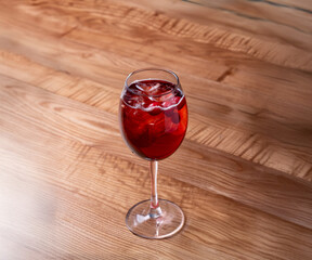 A tall wine glass with a vibrant red cocktail, served on a wooden table. Possibly a fruity, refreshing beverage.
