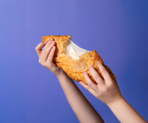 Hands tearing apart a crispy, golden Cheburek with a stretchy filling, set against a bright background. A traditional fried pastry from Eastern European and Central Asian cuisine.