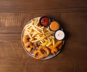 A plate of crispy fried squid rings and French fries with assorted dipping sauces, displayed...