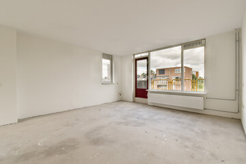 A bright, empty room featuring large windows that let in natural light. The space has a bare concrete floor and an inviting atmosphere for future decoration.