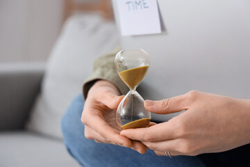 Woman with hourglass and laptop at home, closeup