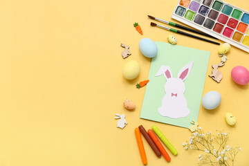 Paper bunny with Easter eggs, markers, watercolor paints and beautiful gypsophila flowers on yellow...