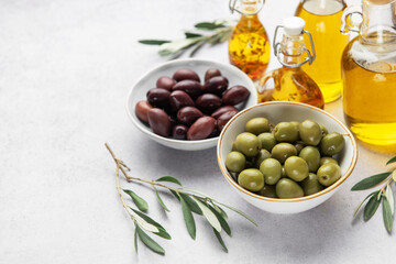 Bowls of green and black olives with olive oil bottles and olive branches