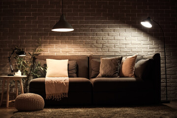 Stylish interior of living room with comfortable sofa, pouf and glowing lamps