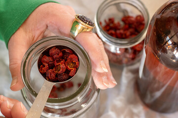 A woman prepares a rosehip oil infusion using dried rosehips and jars.
