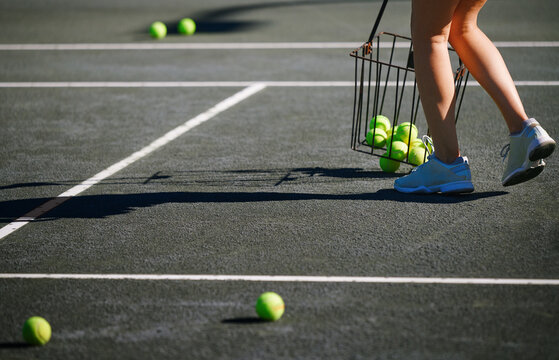 Woman collecting tennis practice balls into the basket