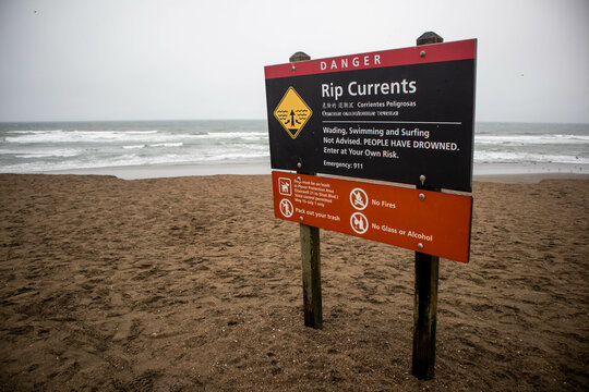 Rip current warning sign on Ocean Beach, ocean waves in background.