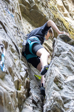Young boy rock climbing with safety gear on a rugged outdoor cliff.