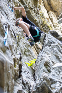 Young boy rock climbing with safety gear on a rugged outdoor cliff.