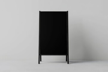 A-frame sign mockups featuring a simple, minimalistic design. The mockup shows a flat lay, front view of a black poster on an A-frame sign stand, placed on a solid grey background with a grey floor.