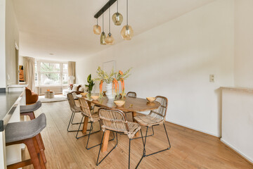 A bright and modern dining area featuring natural wood flooring, elegant lighting fixtures, and stylish rattan chairs complemented by floral decor.