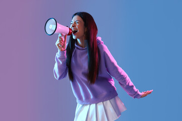 Stylish young woman in hoodie shouting into megaphone on color background