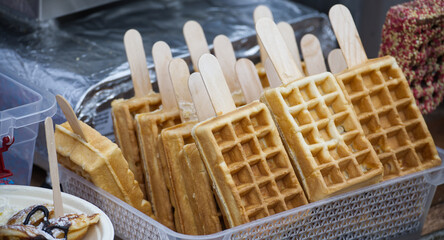 Several delicious Belgian waffles on a stick are displayed and ready to be served at a food market.