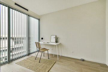 A serene and minimalist home office featuring a stylish chair, small desk, and large windows with vertical blinds that invite natural light.