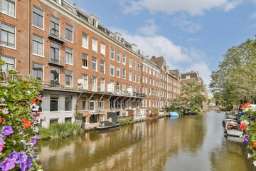 A picturesque scene of traditional Dutch architecture lining a serene canal, adorned with vibrant flowers and a clear blue sky above.