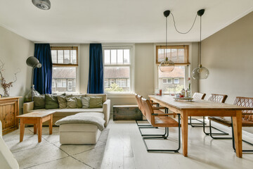 A stylish modern living room featuring a cozy sofa and a wooden dining table, illuminated by natural light from large windows.