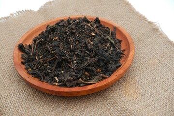 Aromatic black tea leaves in a terracotta bowl on a rustic burlap cloth, emphasizing natural and organic tea preparation.