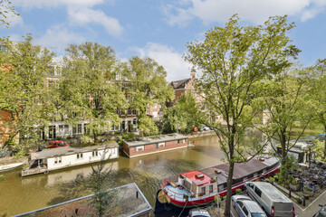 Fototapeta premium A picturesque canal scene showcases lush trees, residential buildings, and colorful boats along the waterway, ideal for relaxation and exploration.