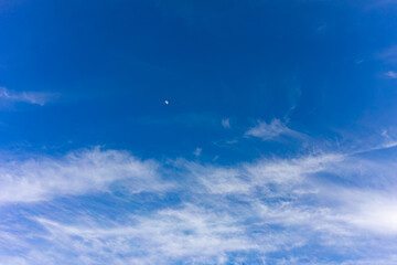 Clear blue sky with white clouds and a crescent moon in daylight