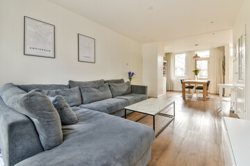 A stylish living room featuring a comfortable gray sofa, a minimalist coffee table, and a dining area adorned with flowers, perfect for relaxation and gatherings.