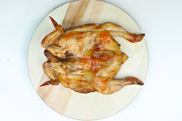 A whole roasted chicken with crispy, golden-brown skin is placed on a round wooden cutting board, displayed in a butterfly-cut style against a plain background.