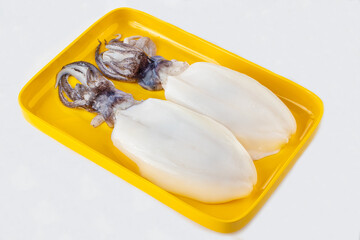 Fresh whole squids on a yellow tray, cleaned and ready for cooking. Perfect for grilling, frying, or making seafood dishes. High-quality and fresh!