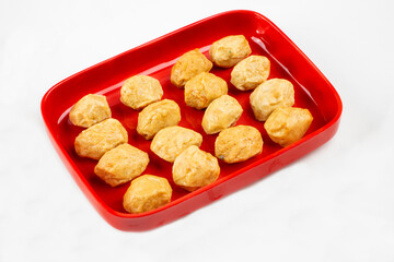A red rectangular plate containing multiple golden-brown fried tofu puffs, arranged neatly. The crispy exterior suggests a light and airy texture.
