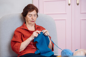 Senior woman knitting in a cozy living room with pastel color accents.