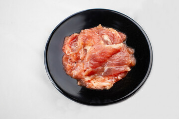 A black round plate with marinated raw chicken, coated in a flavorful sauce, ready for grilling or cooking. The chicken has a reddish-brown color.