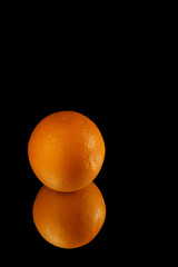 whole orange reflected in a mirror isolated on black background with copy space