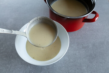 Ladling celery cream soup into a white bowl.