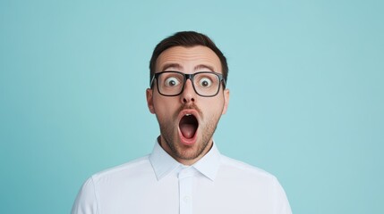 A man wearing glasses exhibits an expression of shock with his mouth wide open, set against a soft blue background. His demeanor suggests an unexpected reaction to something