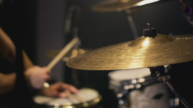 A handsome guy plays drums in a recording studio. Knocks on bronze metal cymbals. Indie artist Create music. Rock style in the school of creativity. Learns to use the drum kit, beats the rhythm. Slow