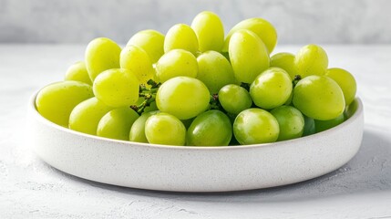 Close up view of a bowl of green grapes on a speckled white surface. The grapes are plump and appear fresh, with a few water droplets visible.