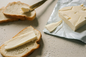 A fresh slice of bread with a thick layer of butter, a butter knife, and scattered salt on a textured surface. Simple and rustic food preparation, highlighting homemade breakfast or snack essentials