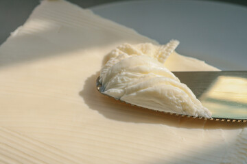 Close-up of a knife spreading fresh butter with soft curls forming on the blade. Warm natural light highlights the creamy texture, creating a rustic and appetizing food scene