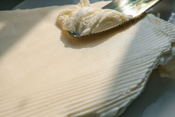 Close-up of a knife spreading fresh butter with soft curls forming on the blade. Warm natural light highlights the creamy texture, creating a rustic and appetizing food scene