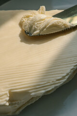 Close-up of a knife spreading fresh butter with soft curls forming on the blade. Warm natural light highlights the creamy texture, creating a rustic and appetizing food scene