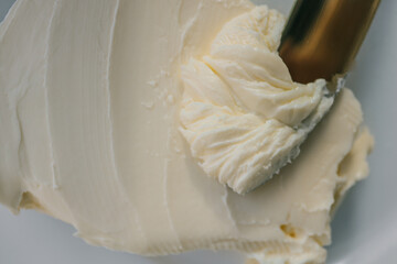 Close-up of a knife spreading fresh butter with soft curls forming on the blade. Warm natural light highlights the creamy texture, creating a rustic and appetizing food scene