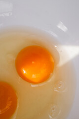 Close-up of raw egg yolks in a white bowl, illuminated by natural light. The golden, glossy texture of the yolks contrasts with the translucent egg whites, creating a fresh and organic food