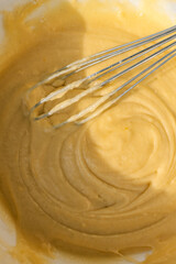 Close-up of a whisk mixing smooth yellow batter in a bowl. The thick, creamy texture of the mixture...