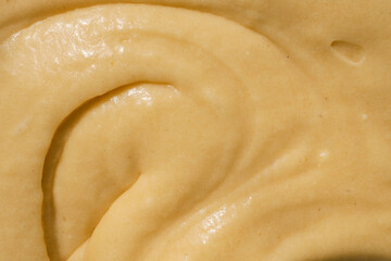Close-up of smooth, creamy batter with a swirled texture. The golden-yellow mixture reflects light, highlighting its thick and glossy consistency, ideal for baking desserts or pastries