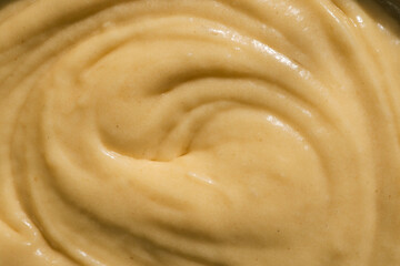 Close-up of smooth, creamy batter with a swirled texture. The golden-yellow mixture reflects light,...